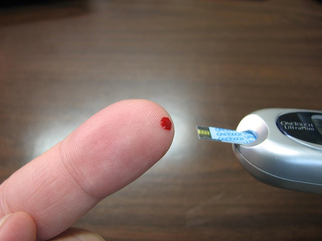 Finger with a drop of blood and a testing device for checking glucose levels