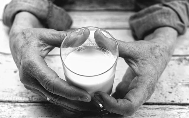 Old hands holding a glass of milk.