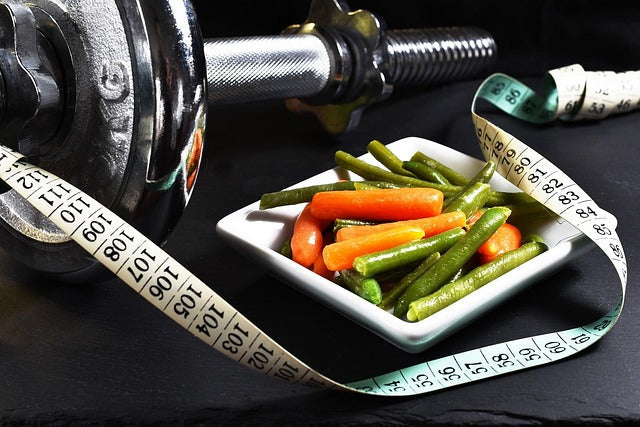 A plate of vegetables alongside a measuring tape and gym weights.